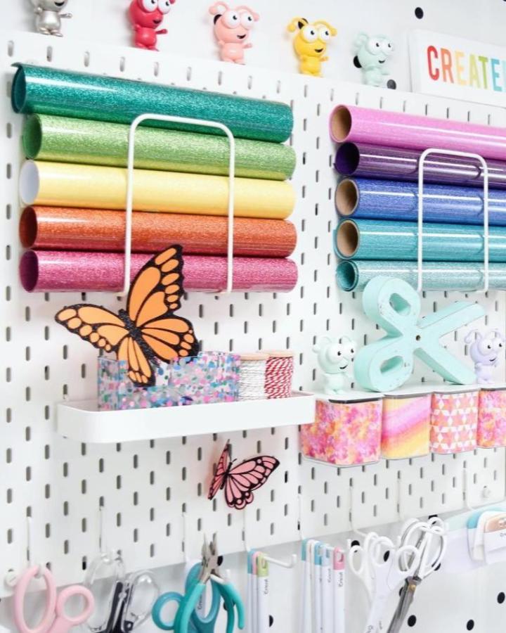 Colorful Ikea Skadis pegboard craft storage from @abbi_kirsten_collections holding rainbow vinyl rolls and crafting tools.