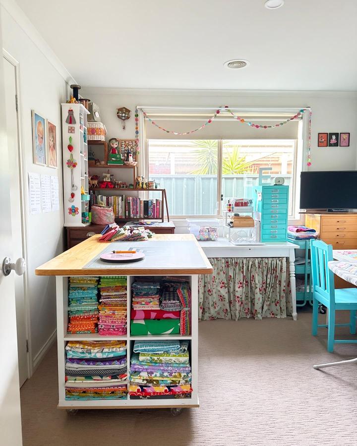 White Ikea Kallax on wheels with colorful fabric stacks and wooden top in a bright sewing room from @emmajeanjansen. ikea sewing room hacks & ideas.