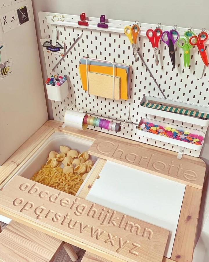 Natural wood personalized kids table with alphabet carving and storage bins from @arthurwears. Ikea flisat table hacks & ideas with pegboard organizer and sensory bin.