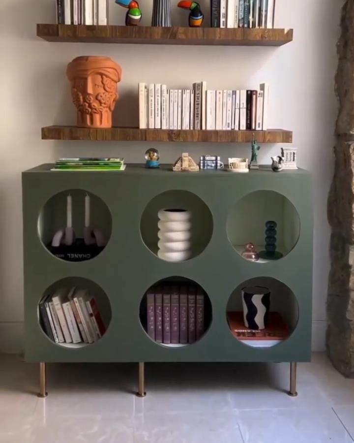 Olive green Kallax with circular cutouts and brass legs from @@archi_zede holding books and decorative objects.