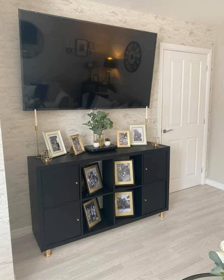 Black matte ikea kallax makeover ideas storage unit with gold details and angled photo frames from @onabudgetofficial in a living room setting