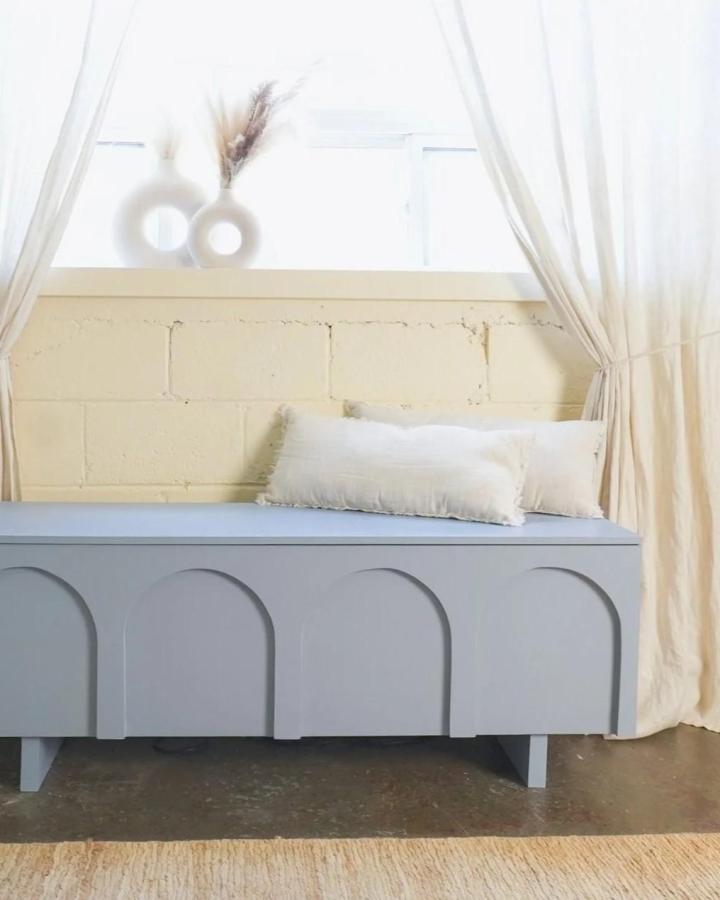 Soft blue Ikea Kallax makeover ideas storage bench with arch details and cozy cushions by The Sorry Girls in bright room.