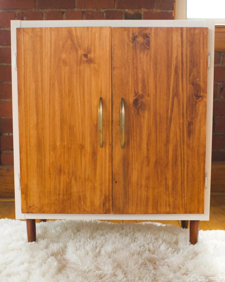 Honey-stained wood midcentury style Kallax cabinet with brass handles and wooden legs from The Sorry Girls. Warm vintage-inspired ikea kallax makeover ideas.