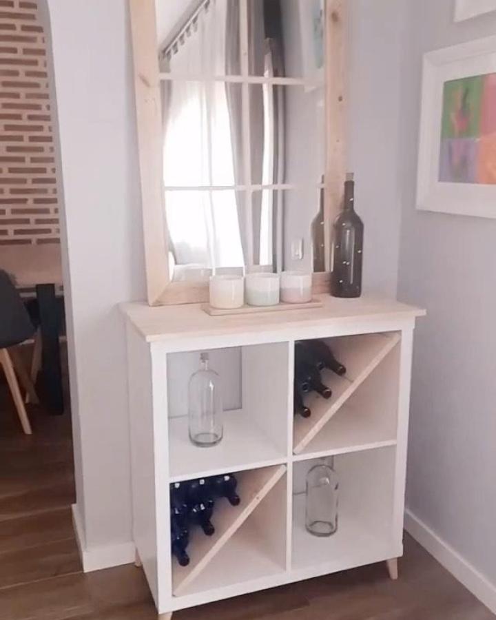 White and natural wood Ikea Kallax styling ideas cabinet from @the.robin.wood with slanted wine bottle dividers and decorative bottles
