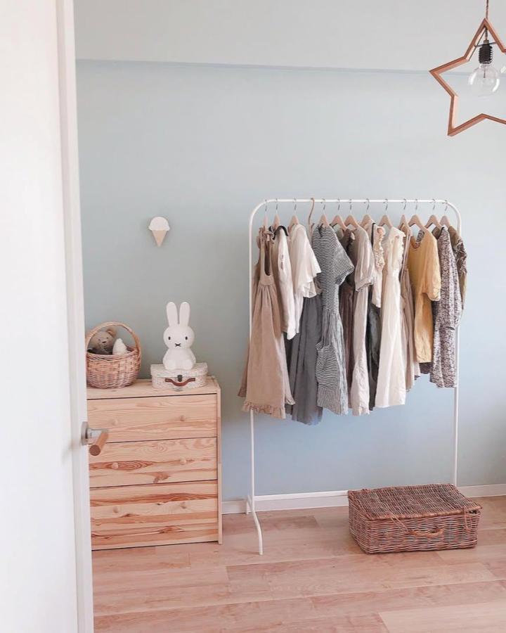 Light blue wall with white metal rack and natural wood drawers in ikea kids wardrobe ideas from @__hochi__m. Soft pastel dresses neatly hung with wicker basket below.
