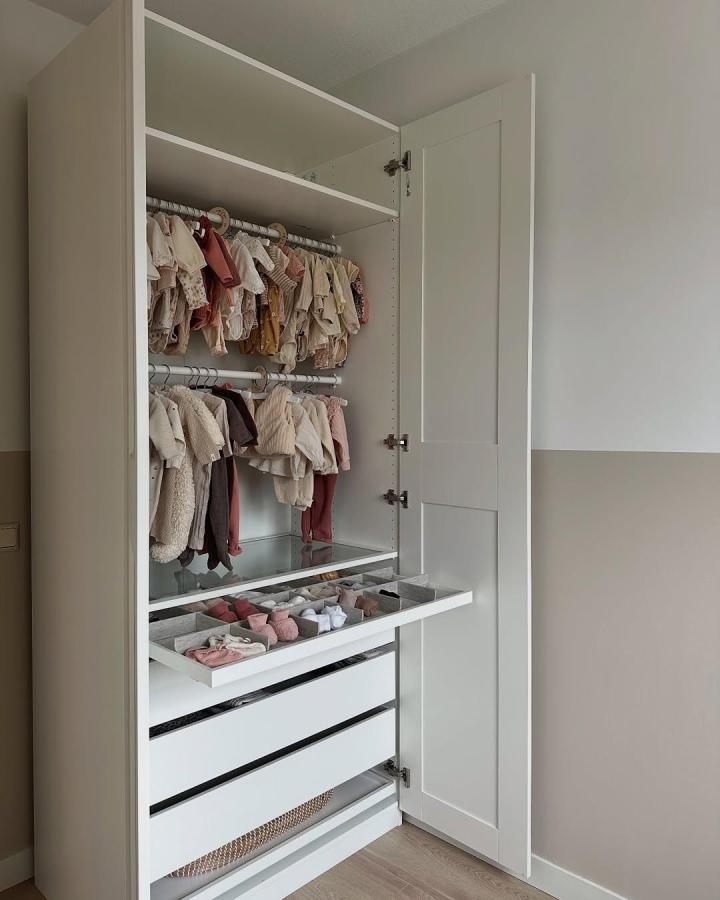 White Ikea PAX wardrobe with clear drawer shoe organizers and double hanging rods from @travelxinterior.bycelien. Neatly arranged kids clothing and accessories.