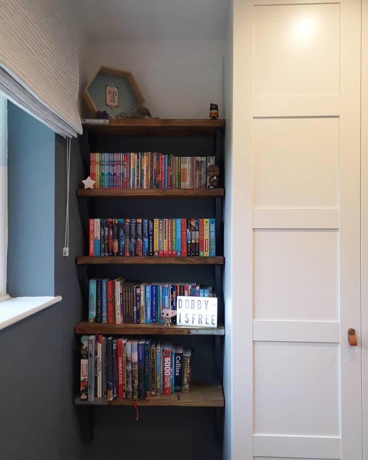 Natural wood floating shelves beside white panel wardrobe from @lilyandthebears. Cozy kids’ book storage space.