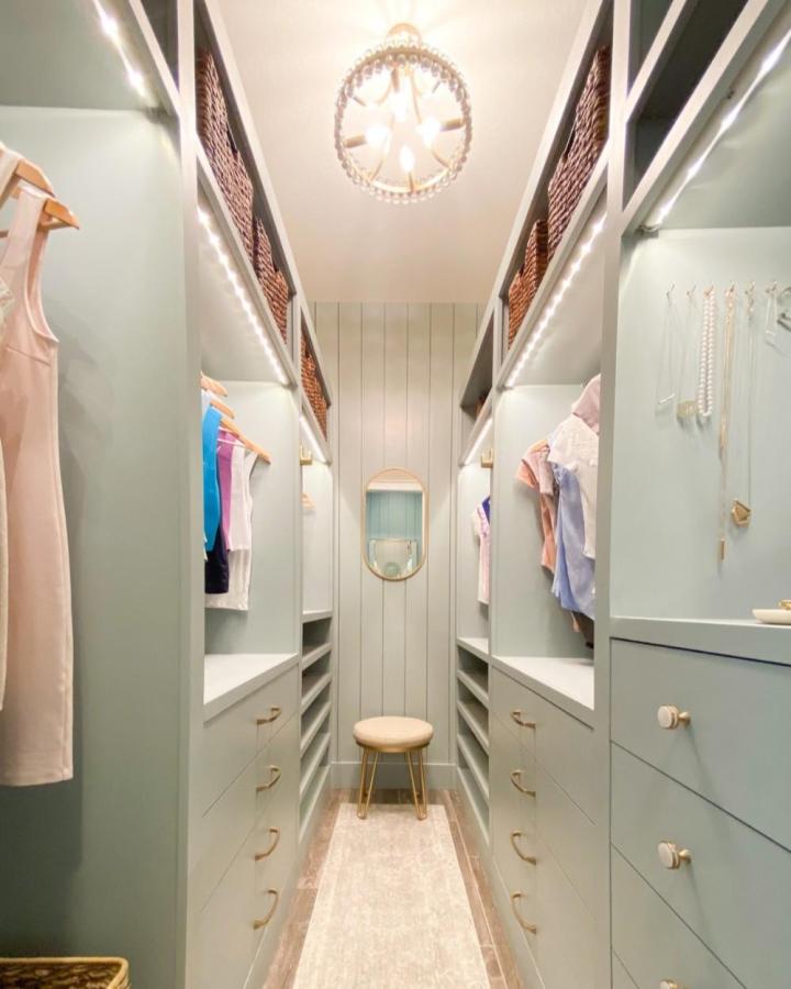 Soft sage green Ikea Pax cabinets in a walk-in closet from Frills and Drills with brass handles and wicker baskets.