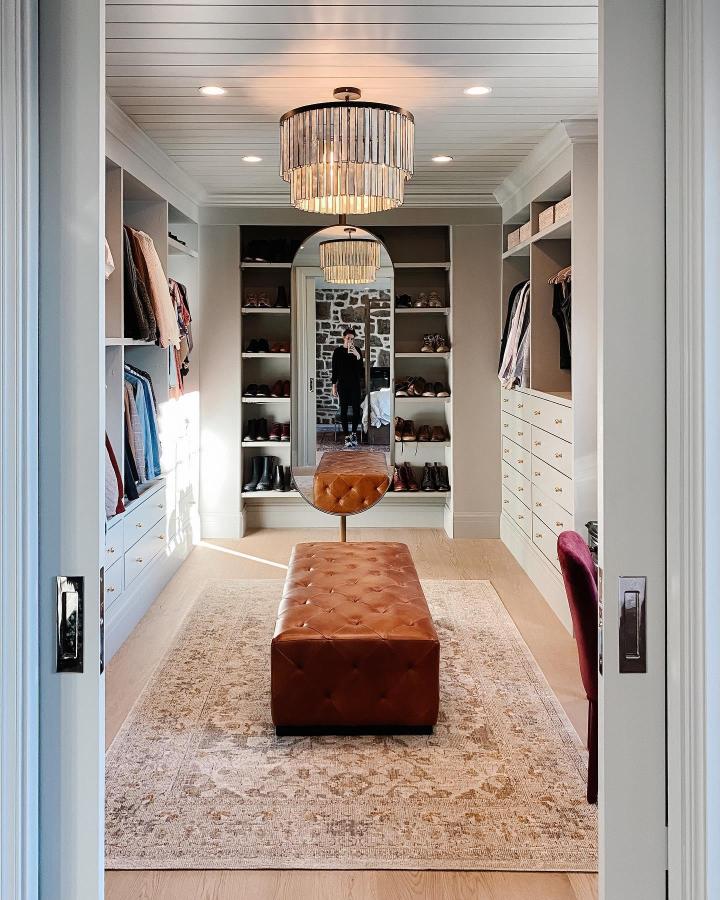 Caramel leather bench and white Ikea Pax closets from @chrislovesjulia cozy walk-in closet with storage and seating.