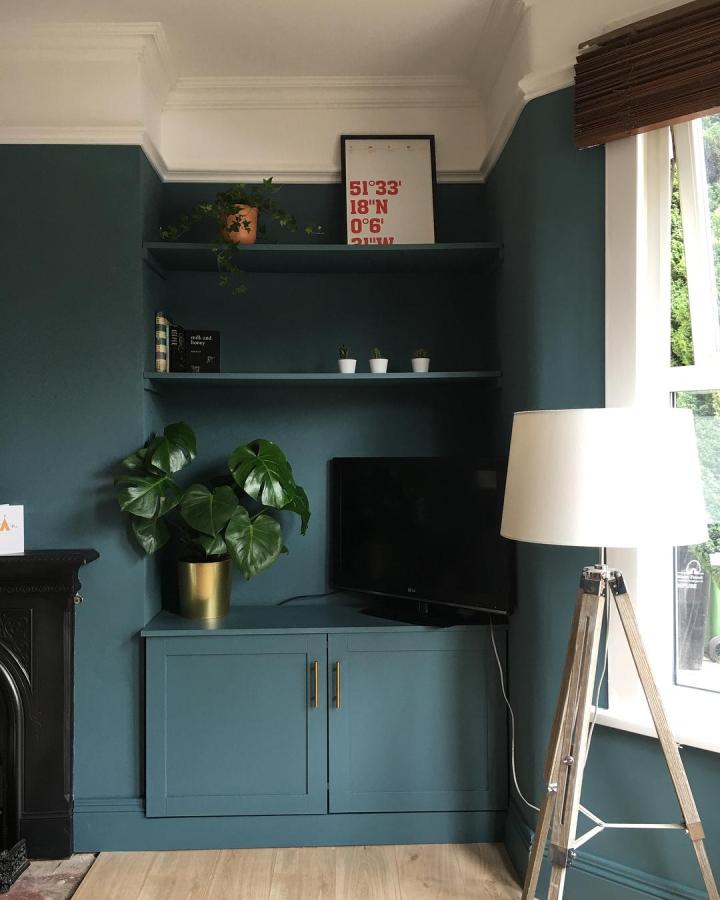 Deep teal painted corner cabinet and shelves with brass handles in a living room from @thealbertproject showing ikea platsa hacks for awkward alcoves.