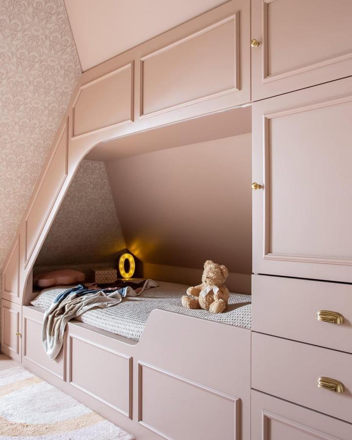 Soft pink built-in bed nook with brass handles from Grey Nest featuring ikea platsa hacks for small bedrooms maximizing storage under sloped ceiling.