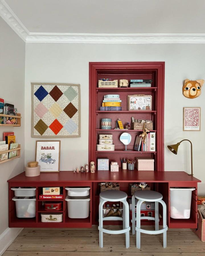 Warm deep red painted Ikea Trofast playroom storage unit from @its_koral_ featuring shelves, bins, and paired gray stools.