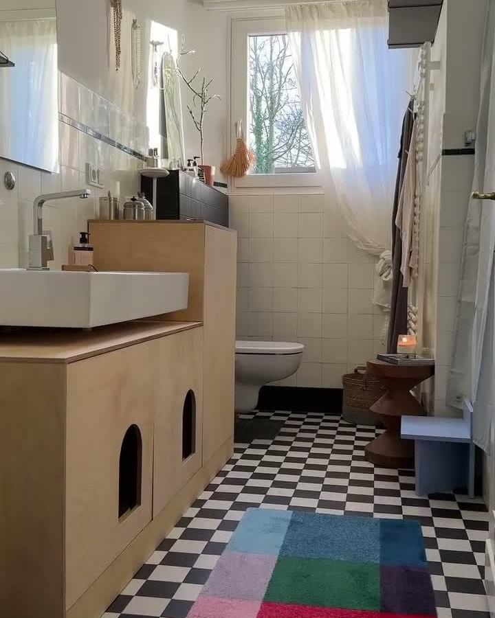 Natural wood paneled ikea besta bathroom vanity ideas with hidden cat litter access by @antoniaschmtz in a bright bathroom with checkered floor and wall-mounted sink