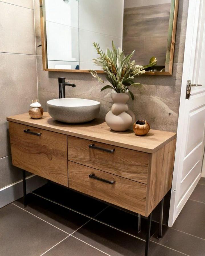 Wood finish Ikea Besta bathroom vanity ideas with black legs and stone vessel sink from The Crafts. Warm and modern bathroom storage solution.