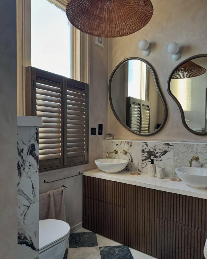 Dark ribbed wood front Ikea besta bathroom vanity ideas in a chic bathroom with marble backsplash and unique mirrors from @iambethmarsden. Elegant and modern.