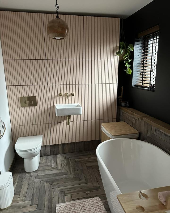 Pale wood paneled bathroom with wall mounted sink and BESTร
cupboards from Zoe Stone. Light wood and brass fixtures create a modern calm aesthetic.