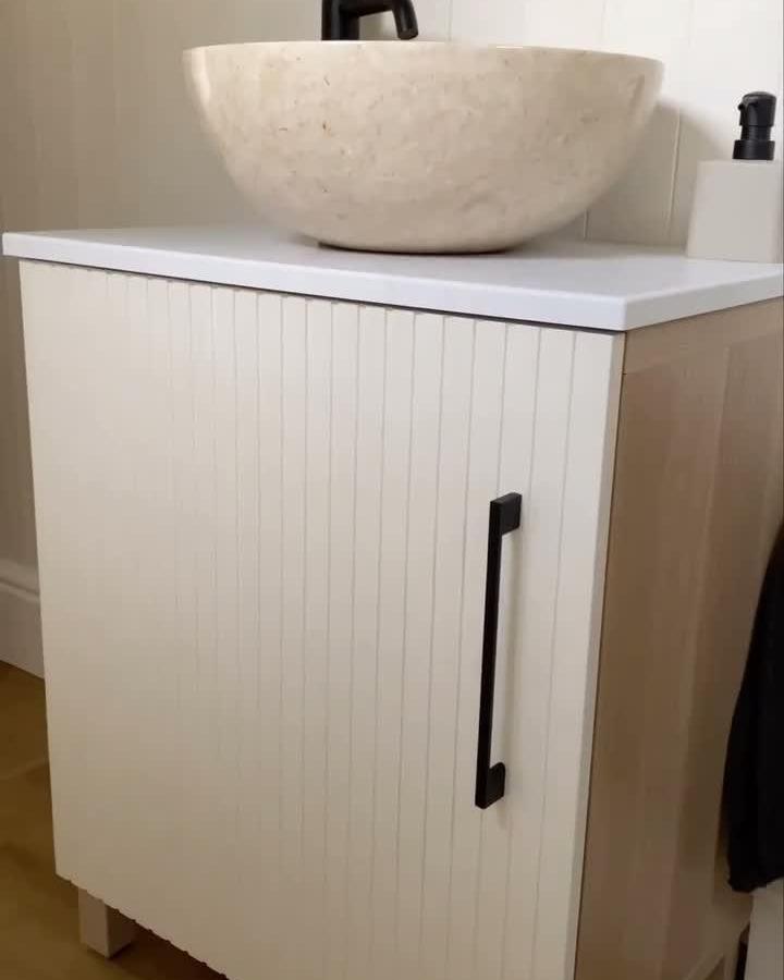 Creamy white upcycled wooden slat front ikea besta bathroom vanity with black handle and natural wood sides from @klk.interiors. Simple elegant bathroom storage hack.
