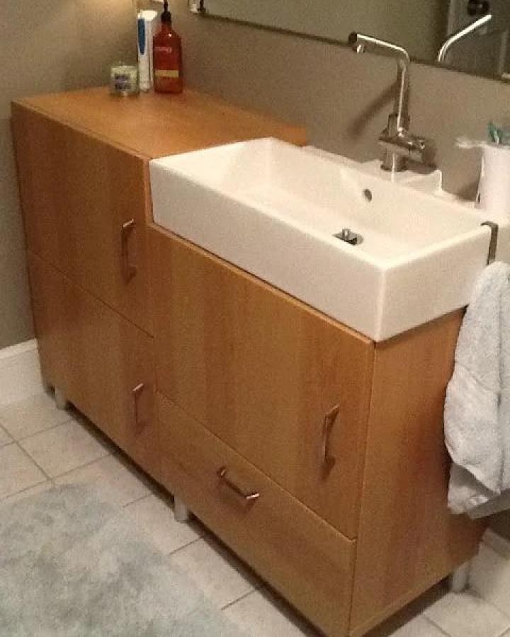 Light brown wooden ikea besta bathroom vanity ideas with a white rectangular Lillangen sink and modern silver faucet in a bathroom corner.