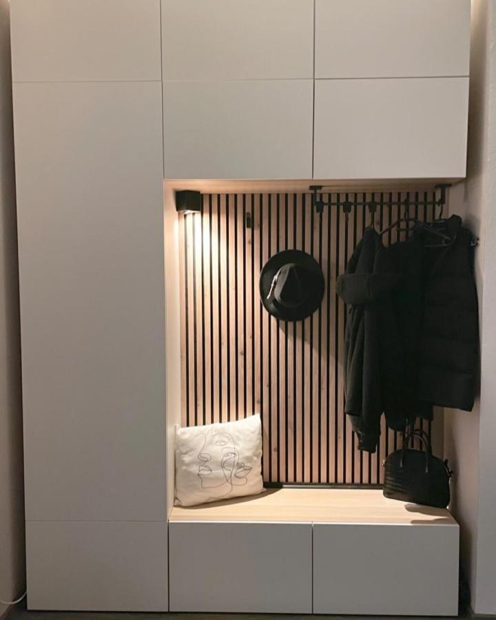 Natural wood slatted vertical panel with white ikea besta bench hack in modern entryway space by @nataliexfr cozy setup with hooks and light