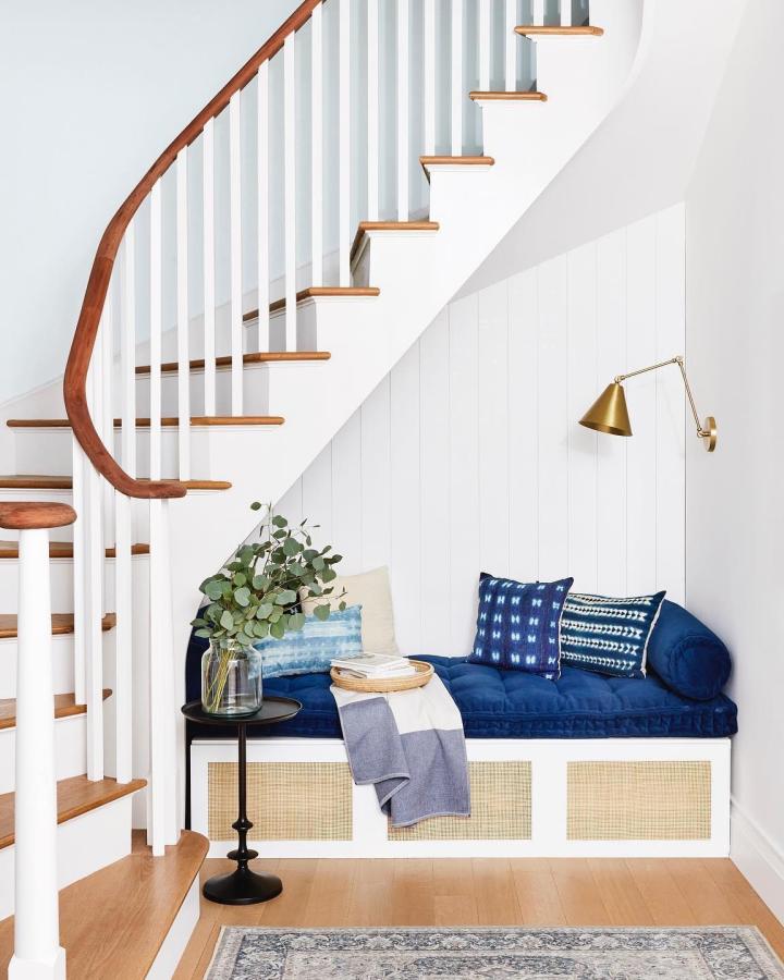 White and cane wood Ikea Besta bench hack under staircase with cozy blue cushion and brass wall lamp from @katieholdefehr.