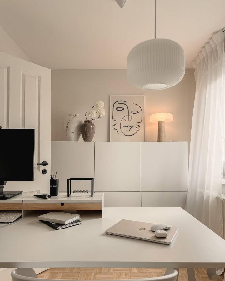 White minimalist ikea besta sideboard hacks in a serene home office with abstract art and soft lighting from @splitlevel.home. Elegant clean storage unit.