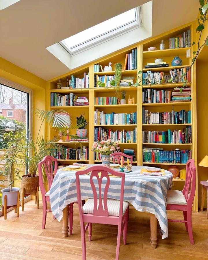 Yellow painted Ikea Billy library wall with angled ceiling and pink chairs in a bright dining room from @thehousethatcolourbuilt. Vibrant ikea billy library wall hacks with plants and books.