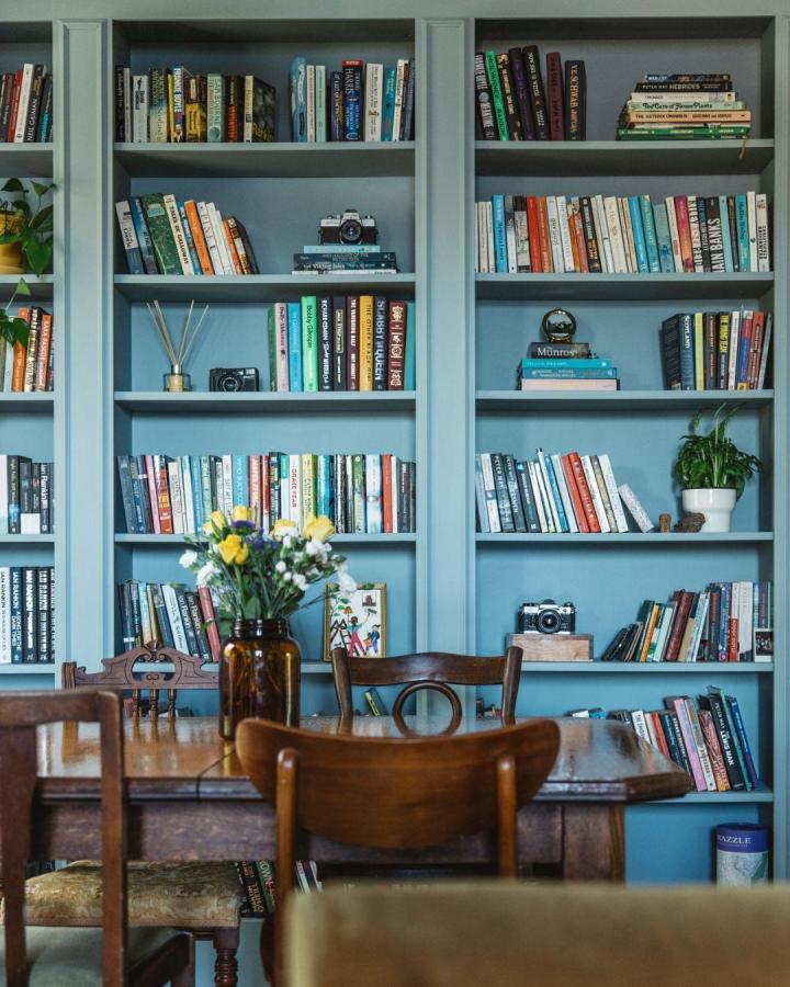 Blue painted Ikea Billy library wall hacks in cozy dining room from @carolinemcquistin. Vintage cameras, plants, and books neatly displayed.
