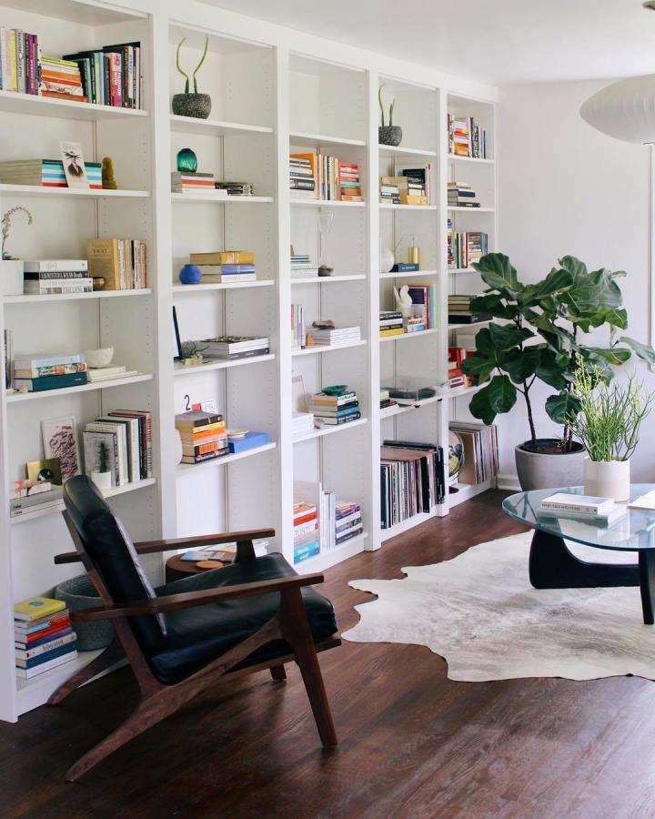 White Ikea Billy library wall with books, plants, and mid-century chair in cozy living room space from @dominomag. Clean minimalist ikea billy library wall hacks.