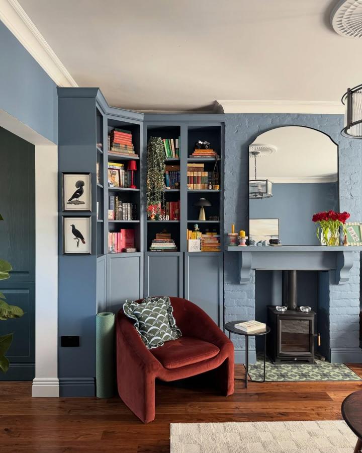 Moody blue painted corner cabinet and shelves in a cozy living area from @therenovation_at_no18 with ikea billy library wall hacks and warm wooden floors.