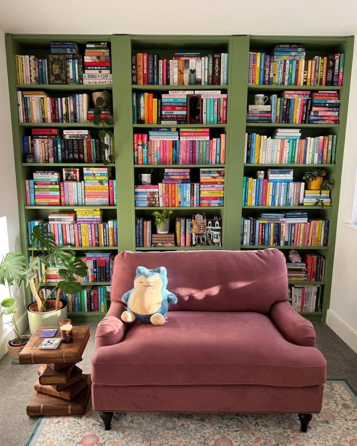 olive green painted ikea billy library wall hacks with colorful books and dusty rose loveseat from @shereadsandtravels. Cozy reading nook with plants and unique side table.