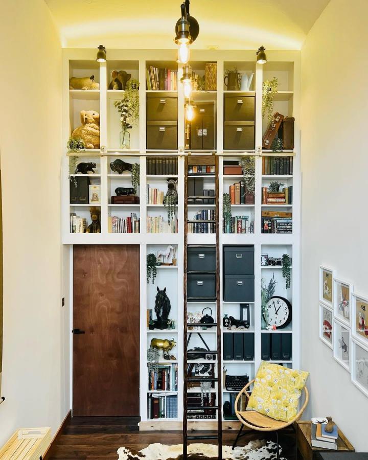 White and charcoal grey Ikea Billy library wall hacks with wooden ladder and greenery by @david.wilson.etc in cozy reading nook.