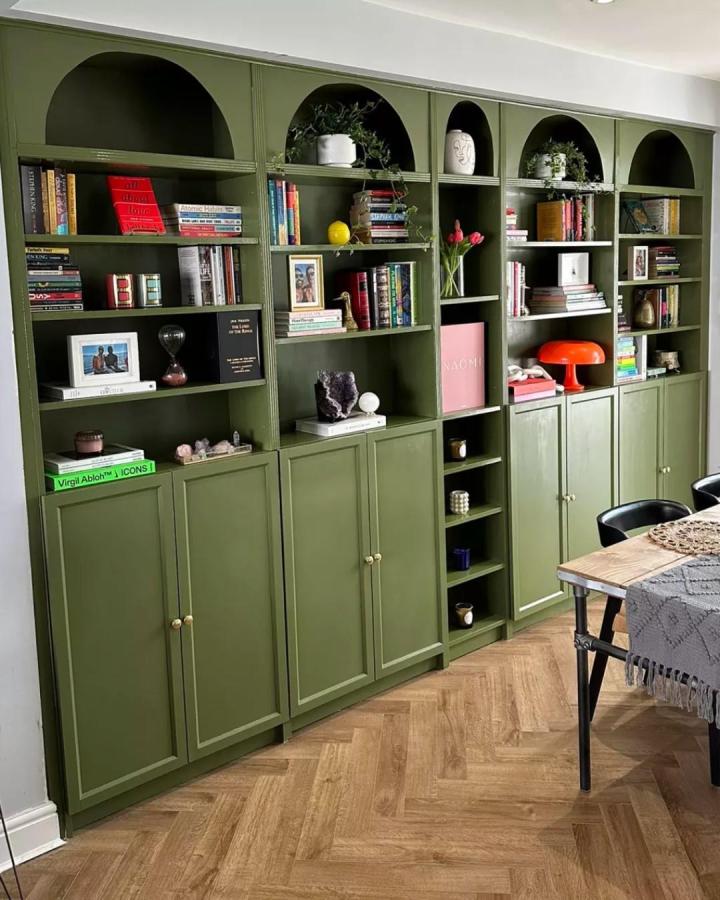 Olive green matte painted Billy library wall hack with brass knobs and arched upper shelves in a cozy dining room from @idealhomeuk designed for stylish storage and display.