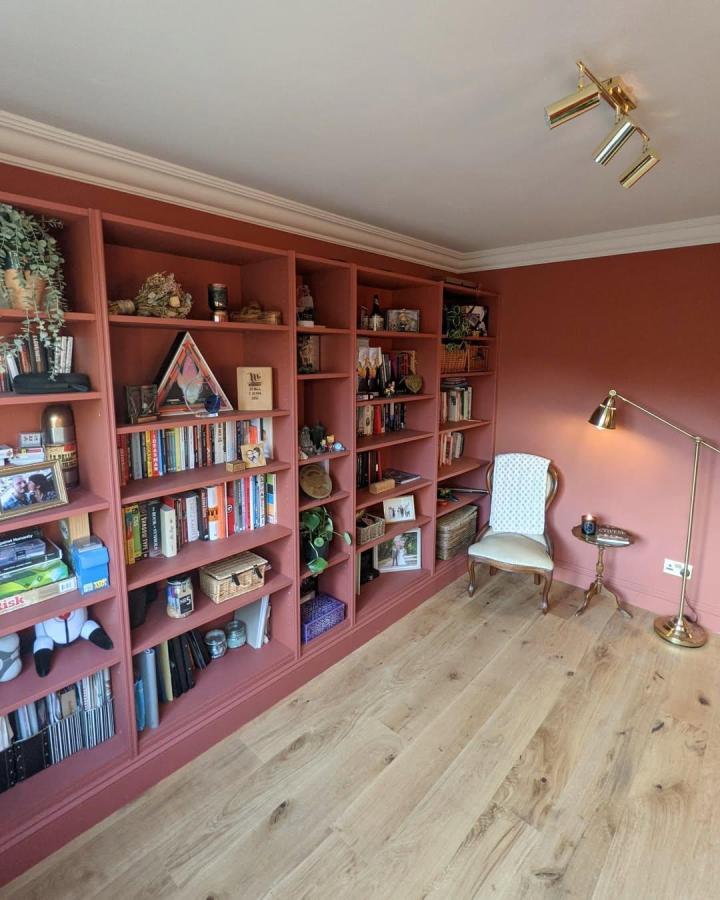 Warm terracotta ikea billy library wall hacks bookshelf in a cozy reading room from @ahousebuiltoncheese with brass lighting and natural wood flooring.