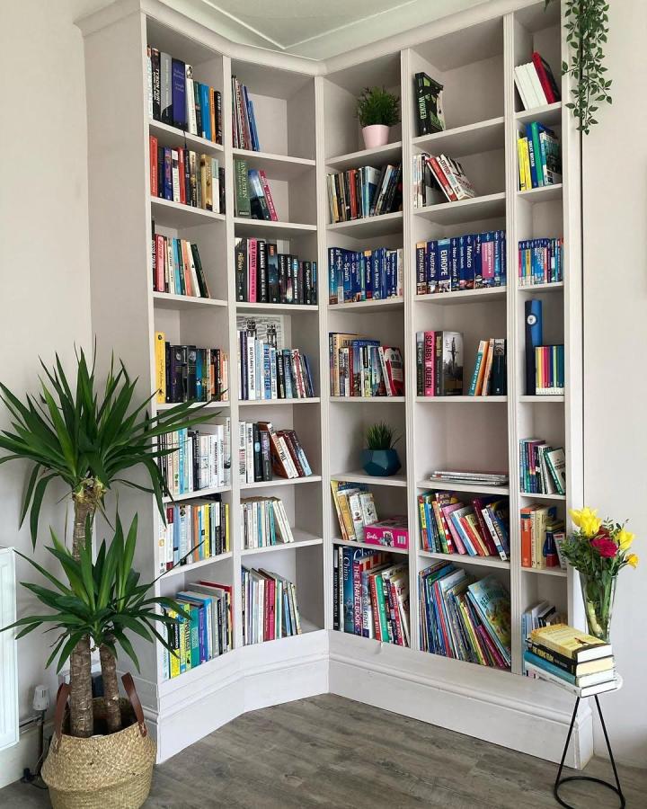 Bright white corner bookshelf with molding and plants from @1930shouserevamp showing ikea billy library wall hacks in a cozy reading nook