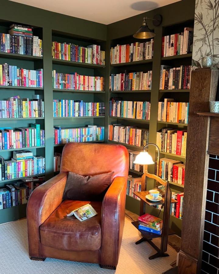 Deep green painted Ikea Billy library wall hack with cozy brown leather armchair and vintage lamp from @justine_in_somerset. Inviting reading nook in a corner.