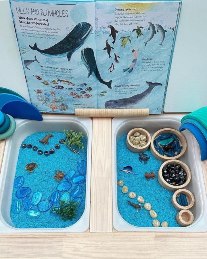 Dyed blue rice sensory table with natural and wooden elements at Ikea Flisat sensory table ideas by @sensoryplaymatters ocean theme setup.