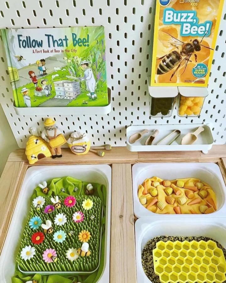 Bee-themed Ikea Flisat sensory table ideas with colorful flowers, felt bees, and honeycomb sensory bins by @playing_the_day_away in a bright play space.