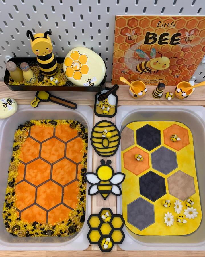 Yellow and orange honeycomb sensory trays with bee toys and themed decorations on Ikea Flisat table from @theplaymatkingdom bright and tactile setup ikea flisat sensory table ideas