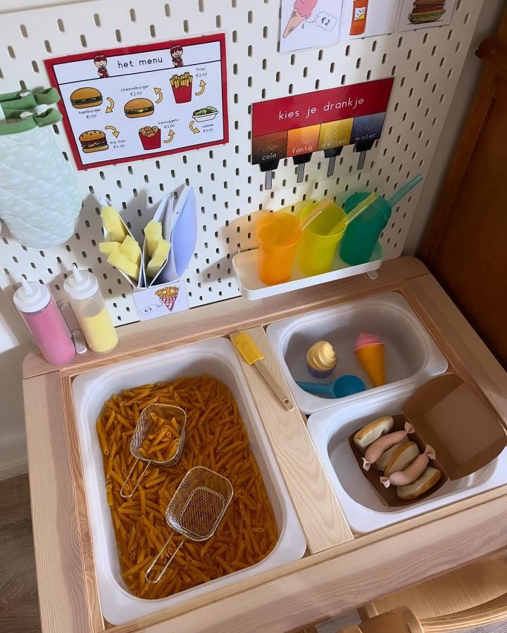 Colorful plastic cups and pretend food on wooden ikea flisat sensory table ideas by @speel_plezier bright and playful setup.
