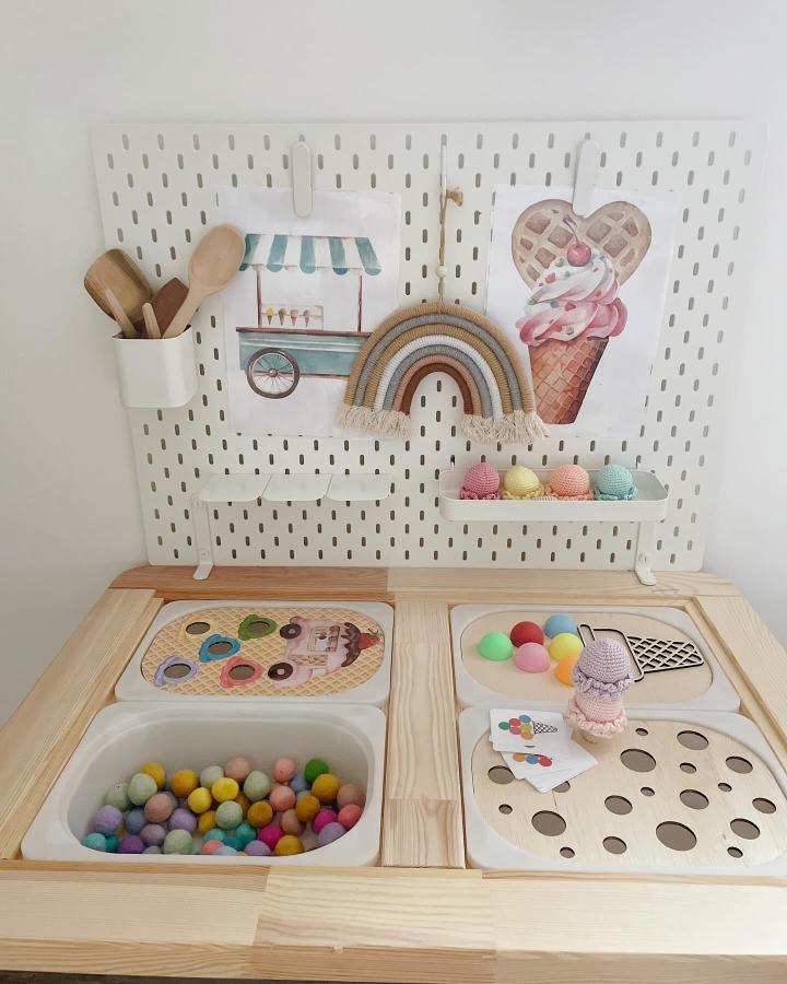 Multicolored felt balls and pastel crochet ice cream on natural wood ikea flisat sensory table ideas from @panna_asztalkaja with pegboard backdrop and utensils.