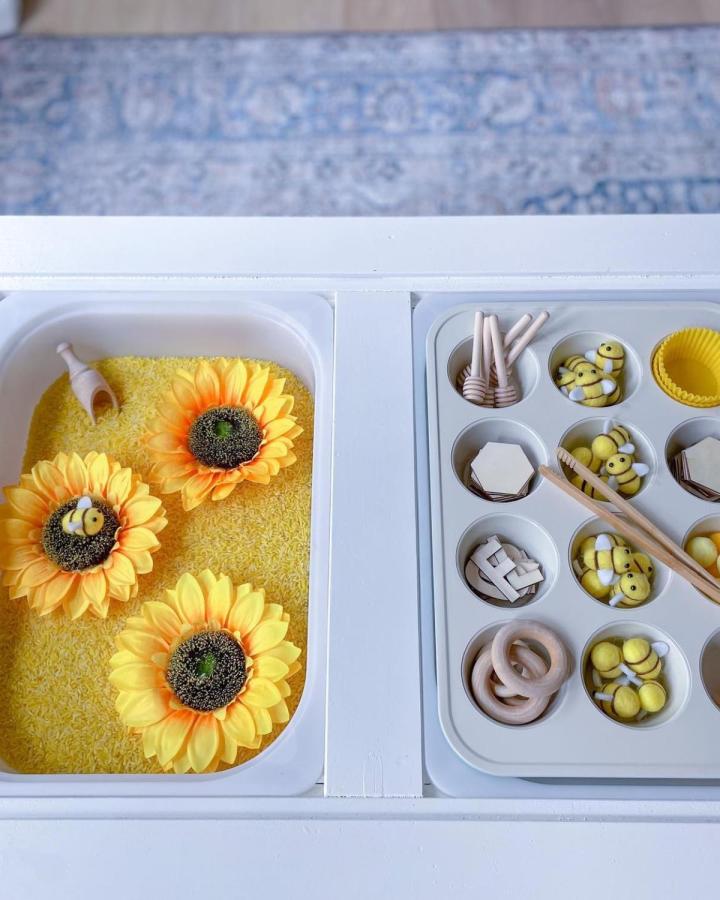 Yellow rice sensory bin and muffin tin with wooden and felt bee toys on Ikea Flisat sensory table by @megbethune.blog bright and cheerful sunflower theme.