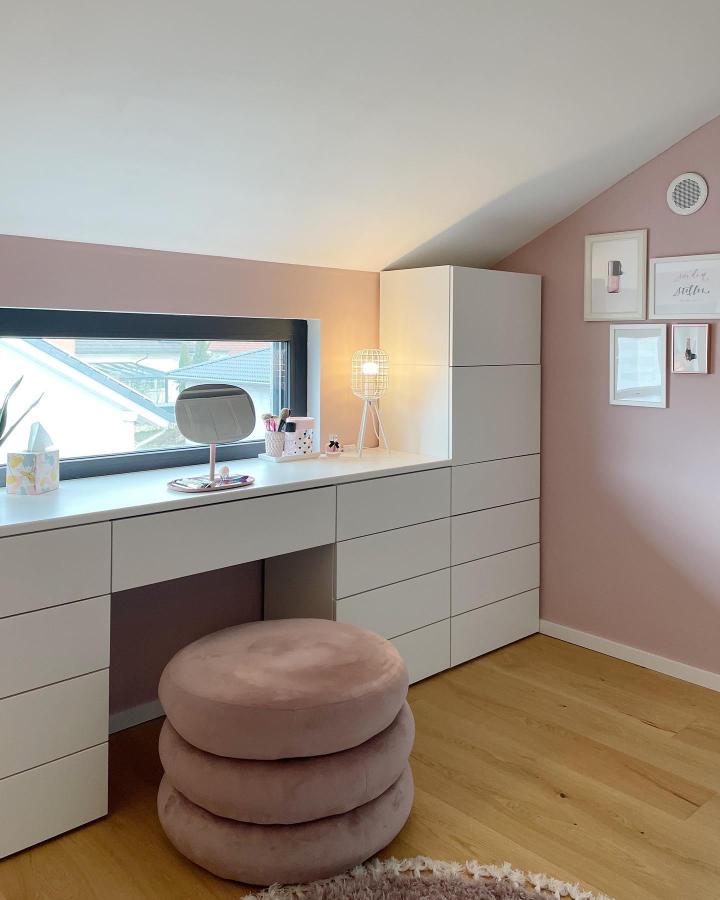Soft pink and white Ikea Platsa wardrobe hacks desk area with layered plush stool and lamp from @whatsandraloves. Stylish storage and workspace under sloped ceiling.