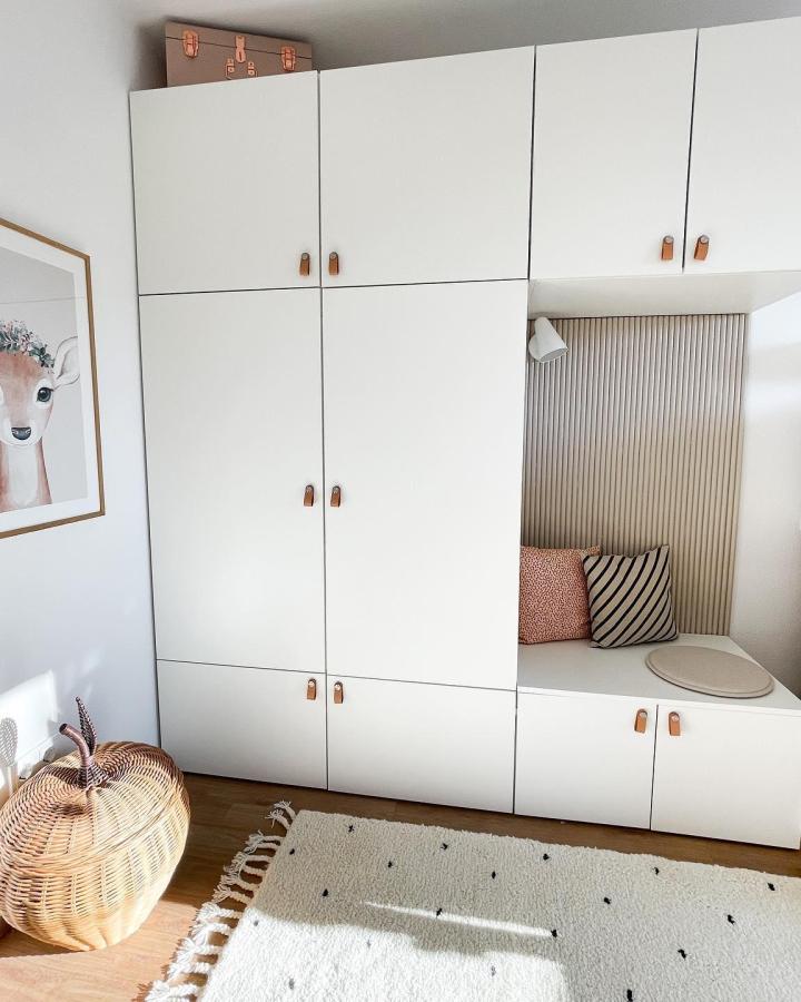 White matte Ikea Platsa wardrobe with leather handles and built-in reading nook by @2anetas_leben featuring slatted wood panel backrest and soft cushions.