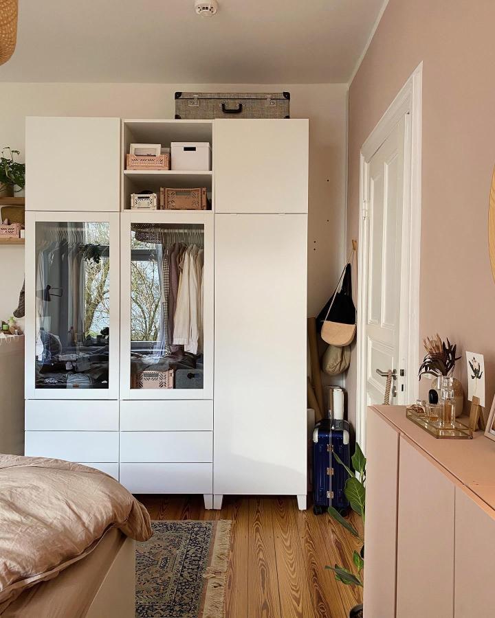 White minimalist Platsa wardrobe with glass doors and open shelves in a cozy bedroom from @inlovewithseptember. Modern storage and display idea for ikea platsa wardrobe hacks.