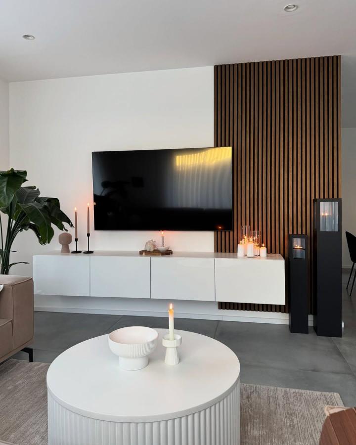 White minimalist floating Ikea Besta TV unit with wood slat accent wall from @naze_dogu in modern living room setting with candles. ikea besta floating tv unit ideas