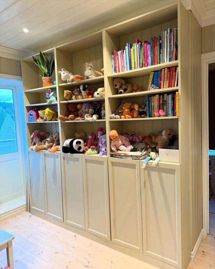 Beige wooden shelving unit with mixed open and closed compartments filled with colorful books and plush toys from @sveitservillasolhaug showcasing creative Billy Oxberg modification.