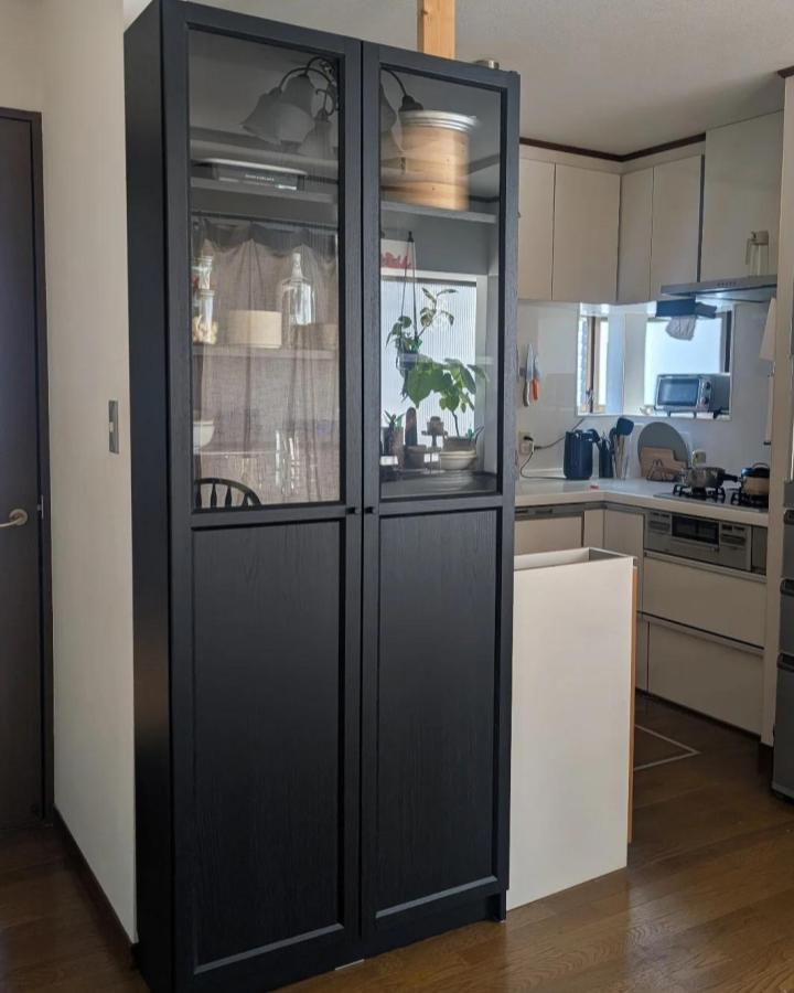 Black framed glass and wood cabinet in a kitchen with plants and ceramics by @uka.home30. Modern storage solution with mixed materials.