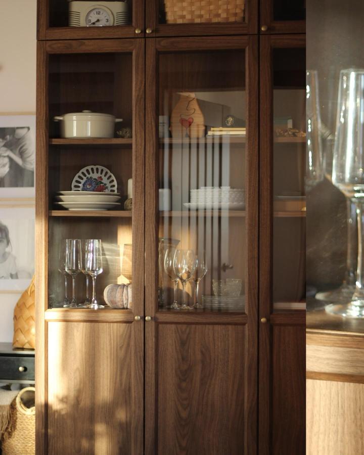 Walnut wood glass-front cabinet with brass knobs displaying dishes and glassware in warm light by @our_little_wooden_house.
