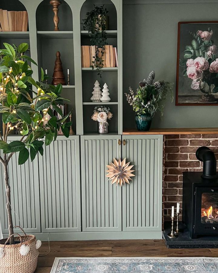 Soft sage green arched bookshelf with fluted doors and wooden decor by @melaniejadedesign in cozy living room setting.