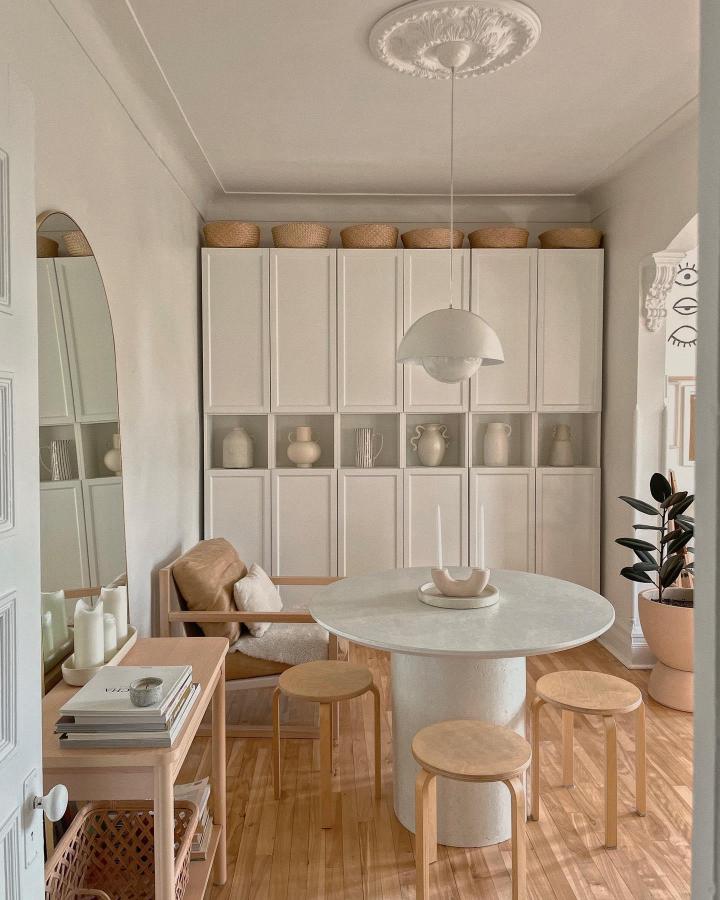 White Ikea storage wall with open mid-shelves and natural baskets from @brookandpeony. Stylish minimalist calm dining space with five stacked units and neutral decor.